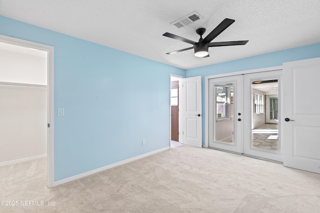 unfurnished bedroom with french doors, a textured ceiling, and light colored carpet