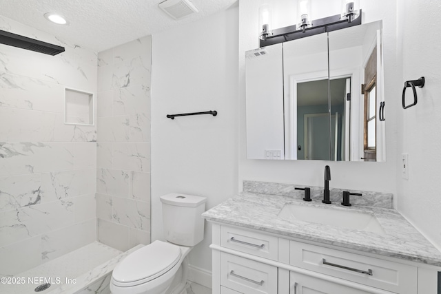 bathroom featuring vanity, tiled shower, toilet, and a textured ceiling