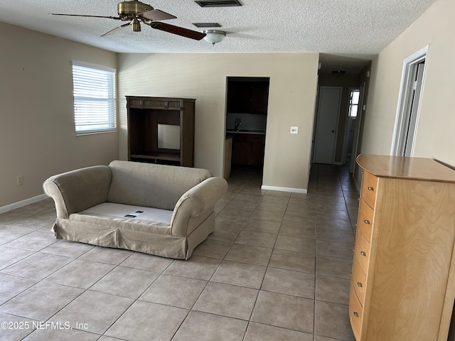 tiled living room featuring visible vents, ceiling fan, a textured ceiling, and baseboards