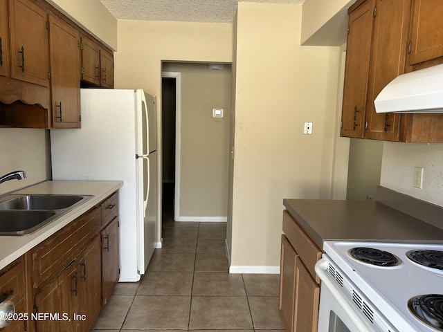 kitchen featuring brown cabinetry, white appliances, a sink, and under cabinet range hood