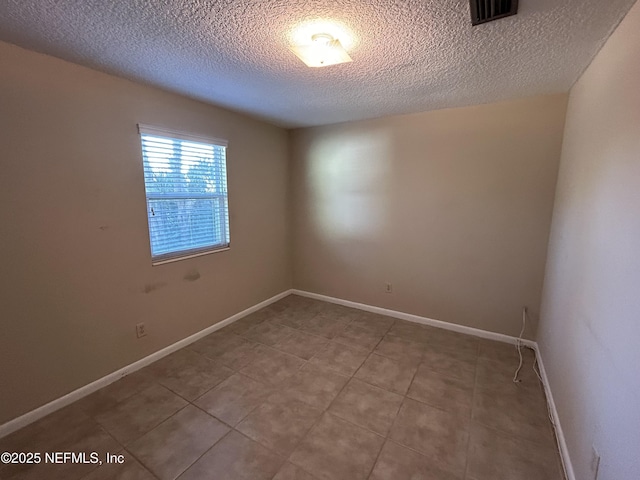 tiled spare room with visible vents, a textured ceiling, and baseboards