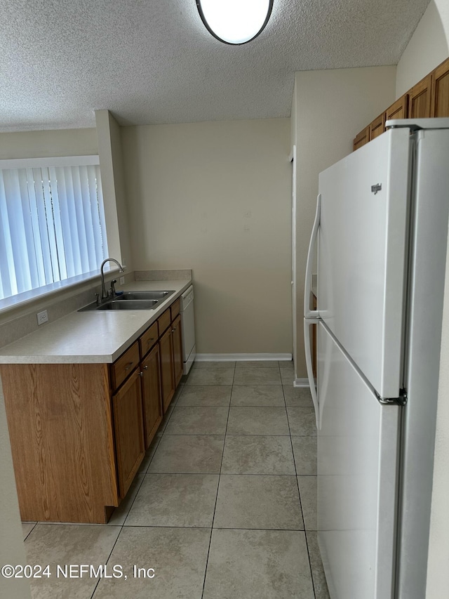 kitchen with light tile patterned floors, white appliances, a textured ceiling, and sink