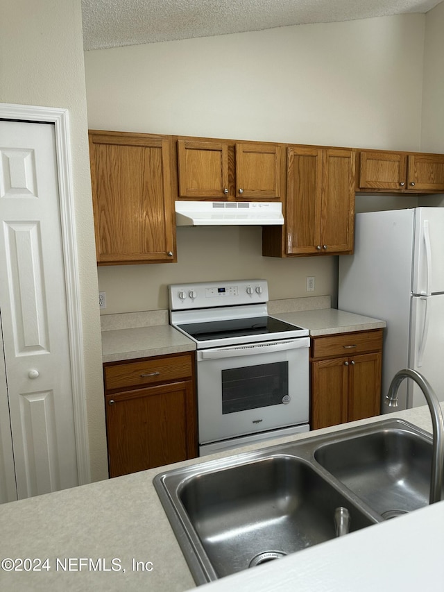 kitchen with a textured ceiling, white appliances, and sink