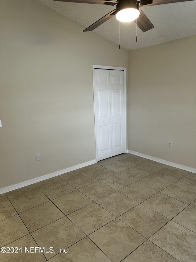 unfurnished bedroom featuring lofted ceiling, ceiling fan, light tile patterned floors, a textured ceiling, and a closet