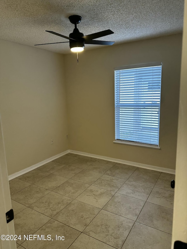 tiled empty room featuring ceiling fan and a textured ceiling