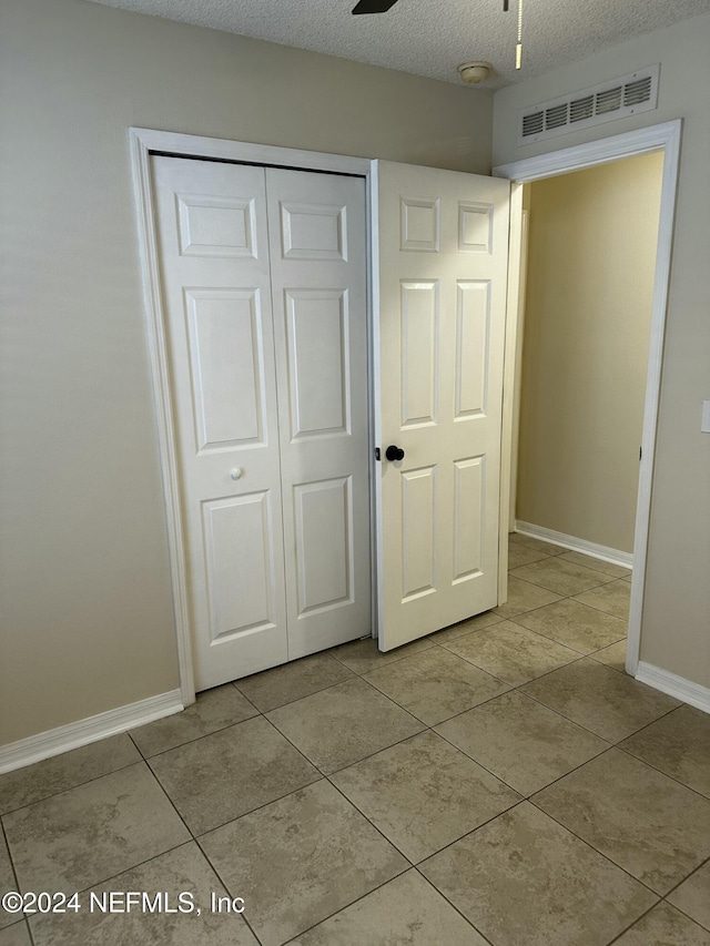 unfurnished bedroom with ceiling fan, light tile patterned floors, a textured ceiling, and a closet