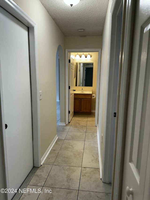 hall with light tile patterned flooring, sink, and a textured ceiling