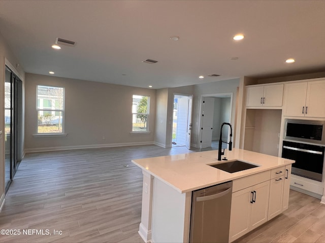 kitchen featuring a center island with sink, sink, light wood-type flooring, stainless steel appliances, and white cabinets