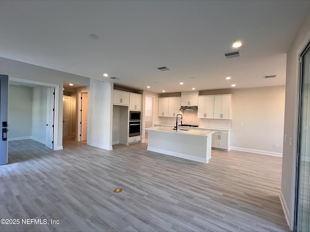 kitchen with white cabinetry, a kitchen island with sink, light hardwood / wood-style floors, sink, and appliances with stainless steel finishes