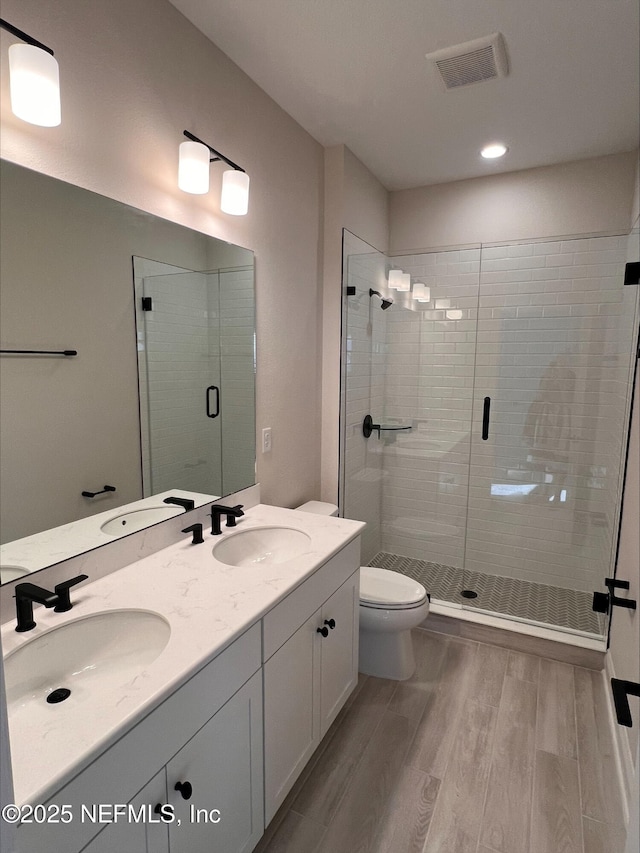 bathroom with toilet, hardwood / wood-style flooring, a shower with shower door, and vanity