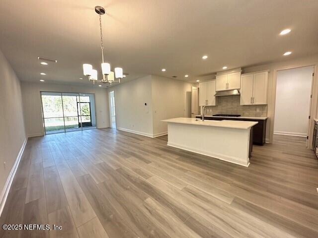 kitchen featuring a kitchen island with sink, hanging light fixtures, backsplash, a notable chandelier, and white cabinets