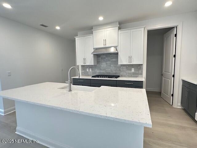 kitchen featuring white cabinetry, a kitchen island with sink, sink, and black gas stovetop