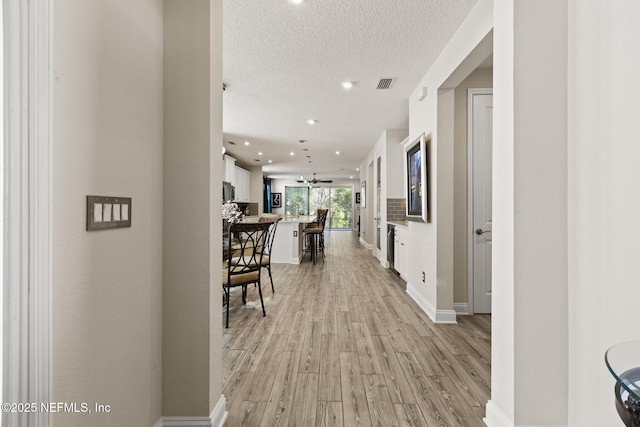 corridor featuring a textured ceiling and light hardwood / wood-style floors