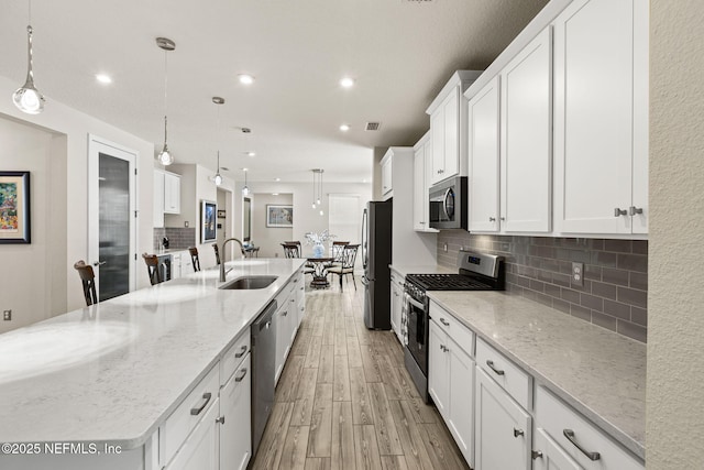 kitchen with appliances with stainless steel finishes, white cabinetry, sink, hanging light fixtures, and a large island with sink