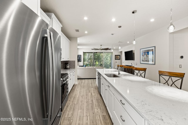 kitchen featuring sink, hanging light fixtures, stainless steel appliances, light stone countertops, and white cabinets