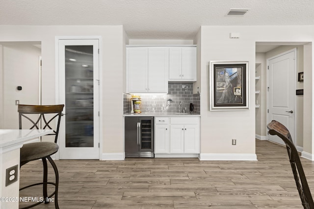 bar featuring white cabinetry, sink, light hardwood / wood-style floors, and beverage cooler