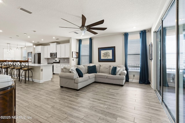 living room with ceiling fan, light hardwood / wood-style flooring, and a textured ceiling