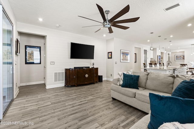 living room with ceiling fan, sink, a textured ceiling, and light hardwood / wood-style floors