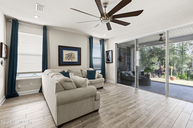 living room with ceiling fan, light hardwood / wood-style flooring, and a textured ceiling