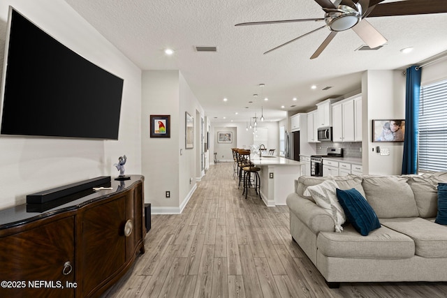 living room with sink, light hardwood / wood-style flooring, a textured ceiling, and ceiling fan