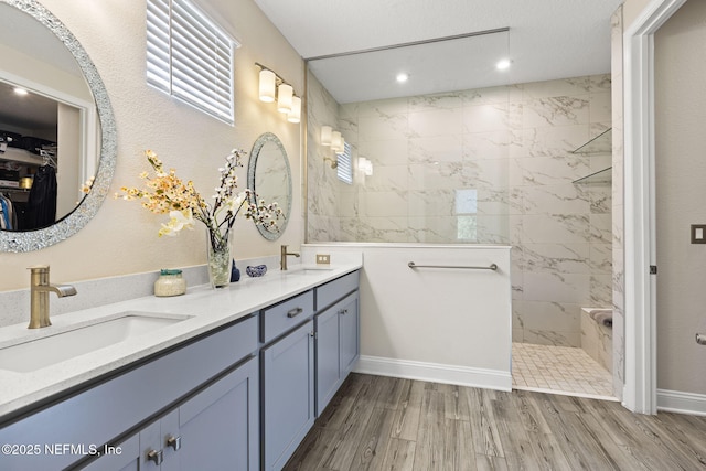 bathroom with wood-type flooring, vanity, and a tile shower