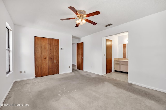 unfurnished bedroom featuring ceiling fan, light colored carpet, a closet, and ensuite bath