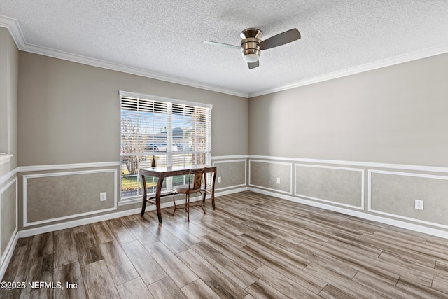 unfurnished dining area featuring a textured ceiling, ceiling fan, crown molding, and wood-type flooring