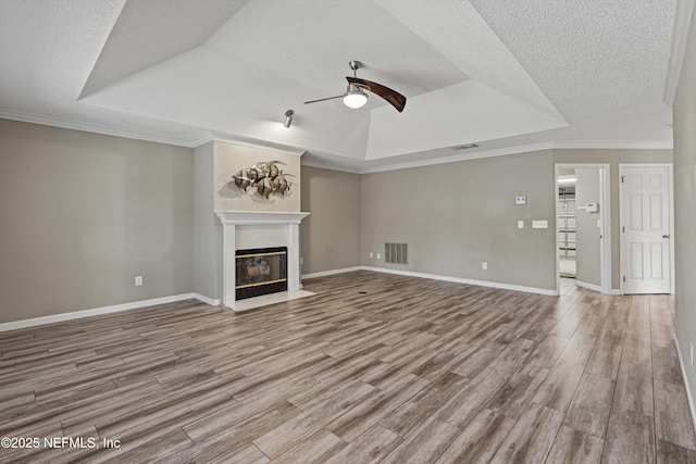 unfurnished living room featuring a raised ceiling, ceiling fan, light wood-type flooring, and crown molding