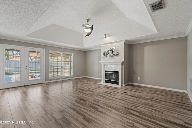 unfurnished living room featuring ceiling fan, a tray ceiling, hardwood / wood-style flooring, ornamental molding, and french doors