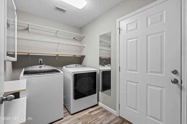 clothes washing area featuring a textured ceiling, separate washer and dryer, and light hardwood / wood-style flooring