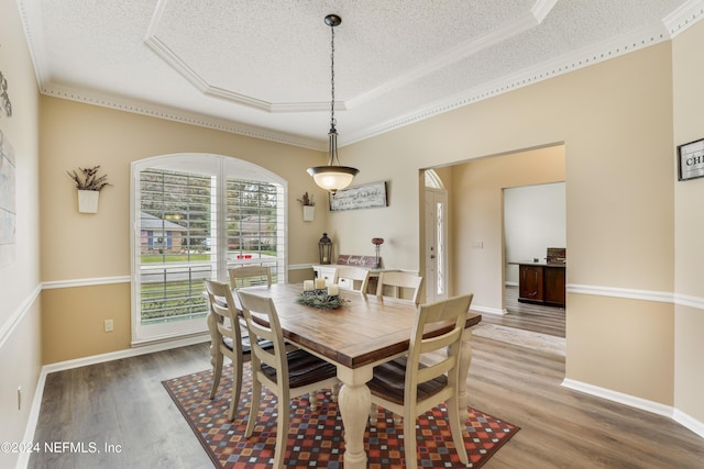 dining room with a textured ceiling, crown molding, a raised ceiling, and hardwood / wood-style flooring