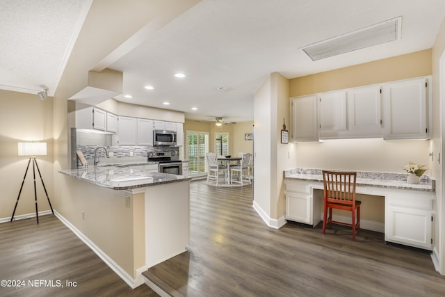 kitchen featuring built in desk, kitchen peninsula, stainless steel appliances, white cabinets, and light stone counters