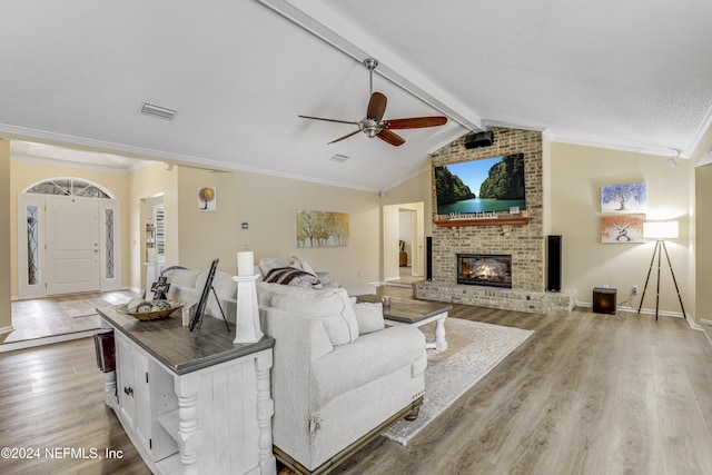 living room with light wood-type flooring, ceiling fan, a fireplace, and lofted ceiling with beams