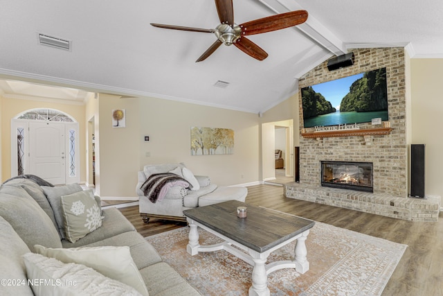 living room with a fireplace, ceiling fan, vaulted ceiling with beams, ornamental molding, and hardwood / wood-style flooring