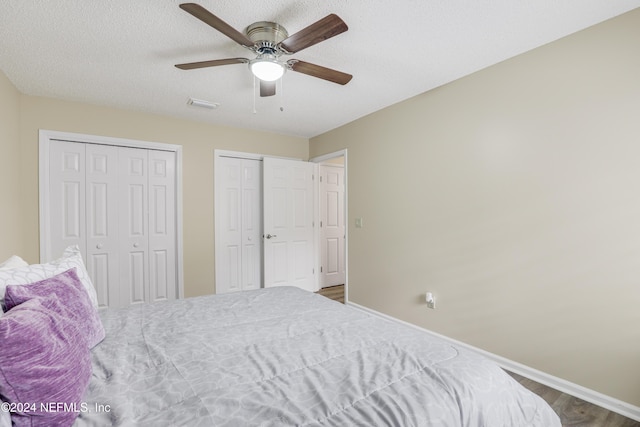 bedroom featuring ceiling fan, multiple closets, a textured ceiling, and hardwood / wood-style floors