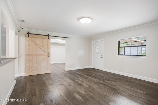 empty room featuring a barn door, dark wood-type flooring, and ornamental molding