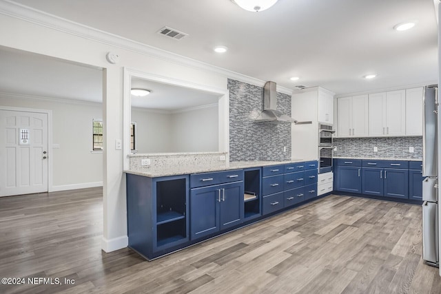 kitchen featuring decorative backsplash, white cabinetry, wall chimney range hood, and blue cabinets