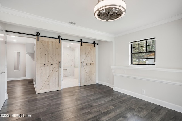 empty room featuring a barn door, dark hardwood / wood-style floors, and ornamental molding