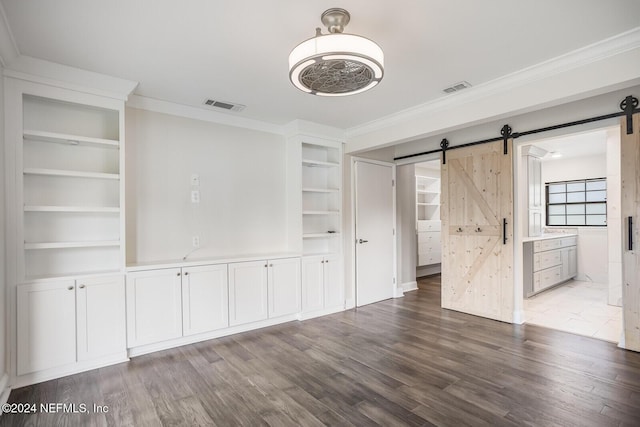 empty room with a barn door, crown molding, and hardwood / wood-style floors