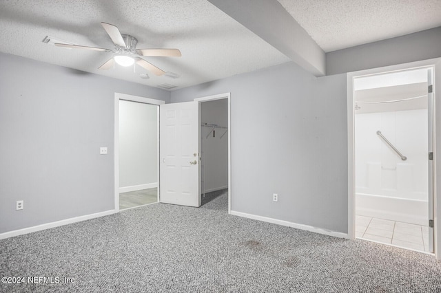 unfurnished bedroom with connected bathroom, ceiling fan, light colored carpet, a textured ceiling, and a walk in closet