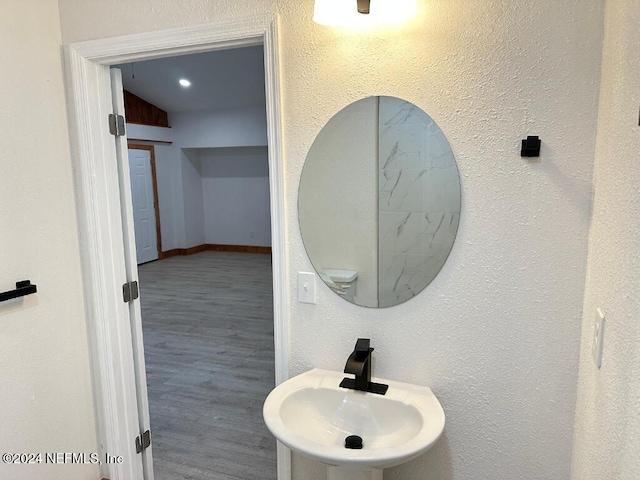 bathroom with wood-type flooring, vaulted ceiling, and sink