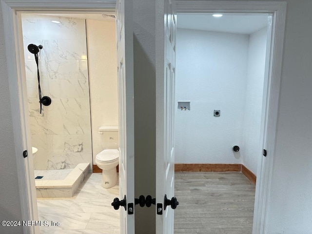 bathroom featuring hardwood / wood-style flooring, toilet, and a tile shower