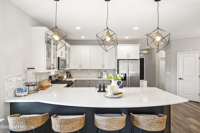 kitchen with dark wood-type flooring, kitchen peninsula, decorative light fixtures, white cabinets, and appliances with stainless steel finishes