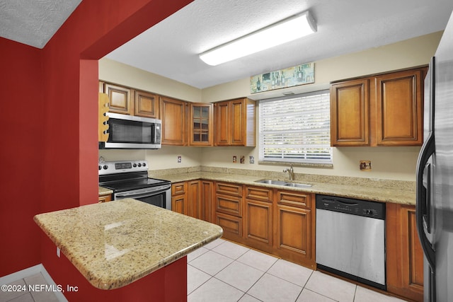 kitchen featuring kitchen peninsula, appliances with stainless steel finishes, light stone counters, a textured ceiling, and sink