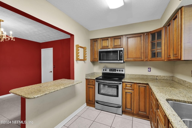 kitchen with an inviting chandelier, light tile patterned floors, light stone counters, kitchen peninsula, and stainless steel appliances