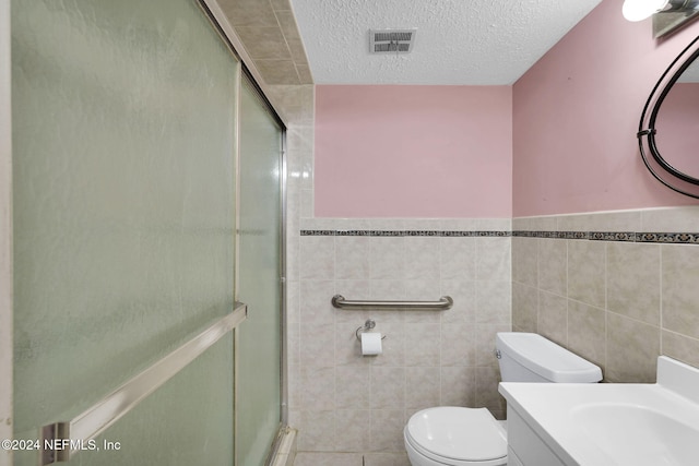 bathroom featuring a textured ceiling, a shower with door, vanity, and tile walls