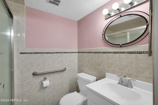 bathroom with vanity, a textured ceiling, toilet, and tile walls