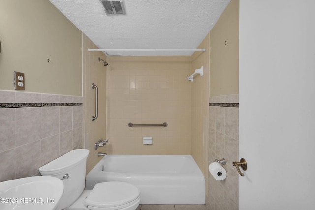 bathroom featuring tiled shower / bath, a textured ceiling, toilet, and tile walls