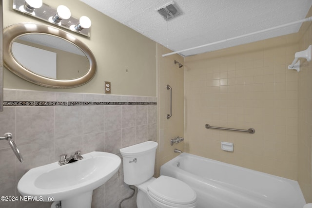 full bathroom featuring sink, tiled shower / bath combo, toilet, a textured ceiling, and tile walls