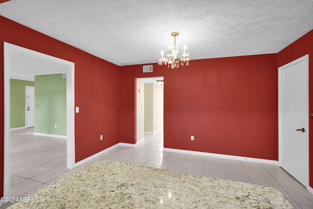 tiled empty room with a textured ceiling and an inviting chandelier